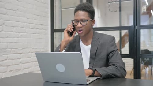 Man Talking on Phone while Using Laptop at Desk