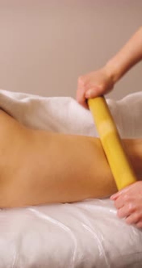 Jovem feliz deitada na cama no salão de spa e desfrutando de massagem com palitos crioulos, cosmetologista
