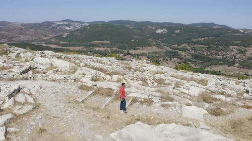 Orbiting drone shot of a local tourist walking around the ruins of the ancient city of Perperikon,