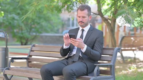 Man Sits on Bench Using Mobile Phone