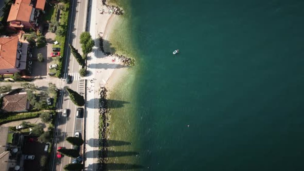 Drone moves forward top-down along Lake Garda shoreline and waterfront ...