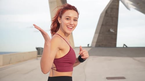 Energetische junge Frau läuft freudig und schaut während ihres Trainings selbstbewusst in die Kamera