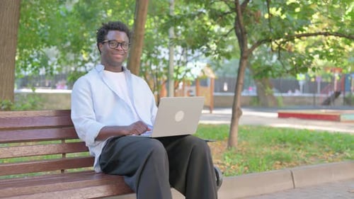 African Man Smiling with Laptop in Park