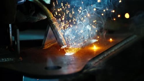 Professioneller Schweißer, der in der Fabrikwerkstatt der Fabrik arbeitet, mit einem männlichen Techniker beim Schweißen