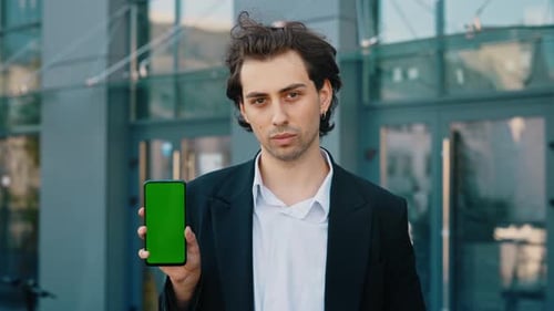 Young Businessman Showing a Smartphone with a Green Screen While Standing Near the Work Place