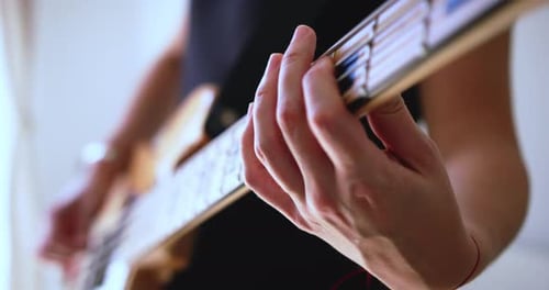 Young woman's hands and fingers playing an electric bass guitar in a recording studio. 4K