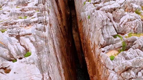 A huge gap among the high rocks filled with water. Dangerous steep cliffs from aerial perspective.
