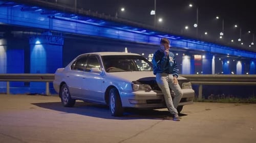 Nighttime Cityscape Featuring Man Leaning on Car Under Bright Lamps City at Dusk with Man in Denim