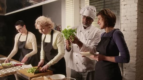 Chef Discussing Fresh Herbs with Woman from Group of Cooking Master Class