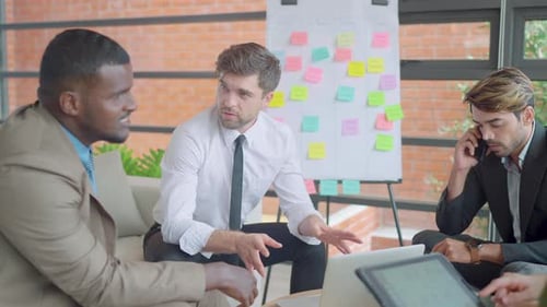 African American business man sit on sofa in meeting area and discuss with Caucasian and Asian team