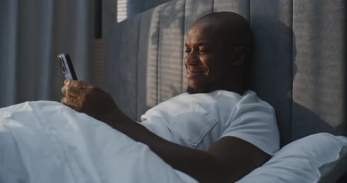 Man Relaxing in Bed Using Mobile Phone