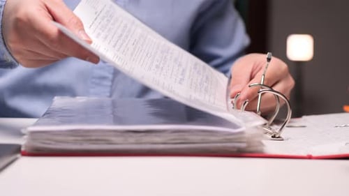Office Worker Filing Documents in a Ring Binder at Night