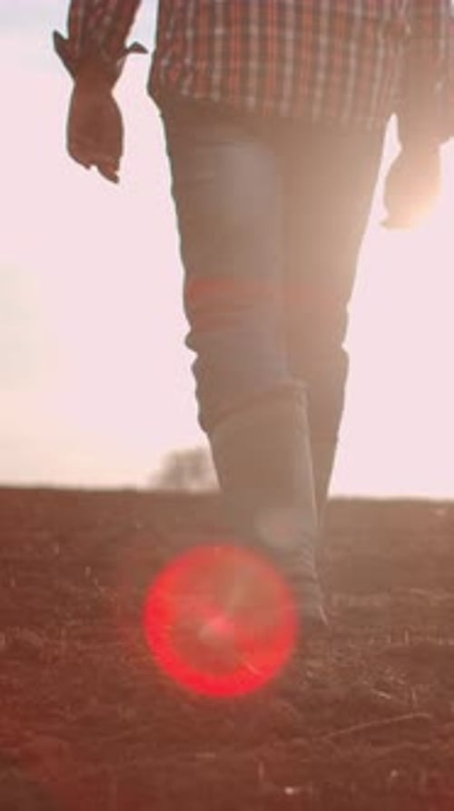 Close Up View of Person in Rubber Boots Walking Across Freshly Plowed Agricultural Field at Sunrise