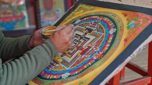 Close-up of an artist painting a traditional colorful thangka on a large canvas near Durbar Square