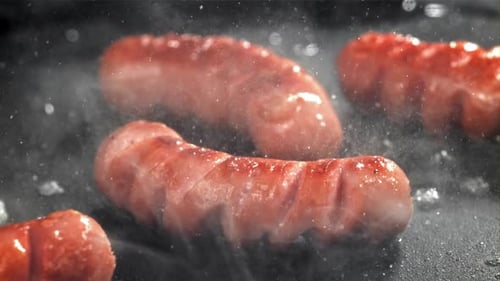 Sizzling sausages cooking on a grill with steam