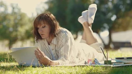 An Adult Woman Lying on the Blanket in the Blooming Park Drawing in Her Sketchbook