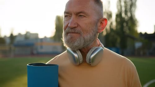Old Caucasian Man Pensioner Looking Around Headphones Holding Mat Sport Stadium Outside Strong
