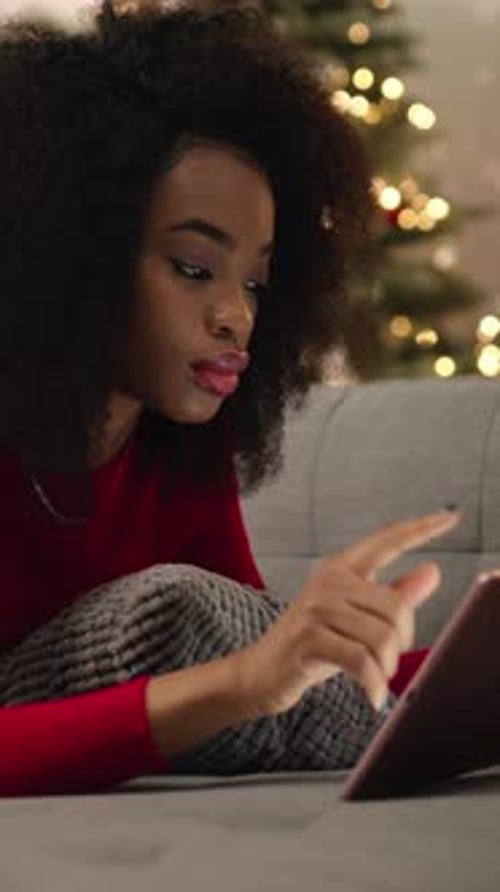 Nice Curly Girl Laying on Sofa Young African Woman Holding Pink Tablet in Hands on Background of