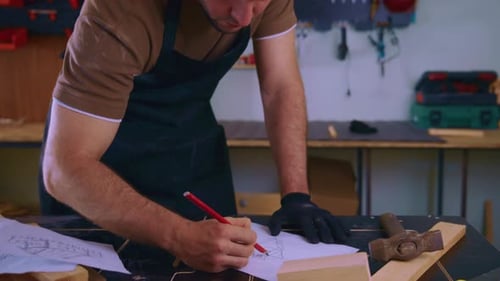Carpenter Drawing Sketch on Piece of Paper in Workshop