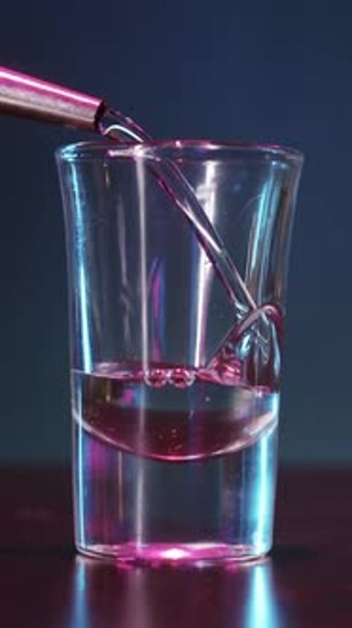 Shot Glass Getting Filled with Liquid Against Dark Backdrop