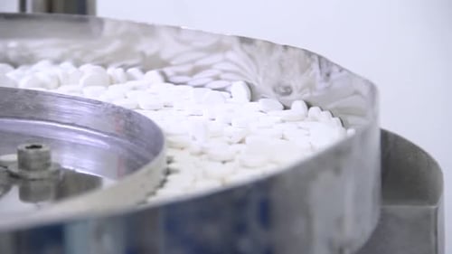 White pills moving on metal automatic line in workshop of pharmaceutical factory