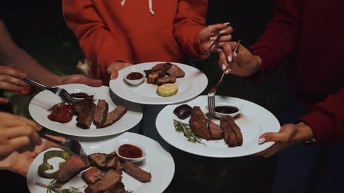 Junge gemischtrassige Freunde aus nächster Nähe stehen mit Tellern im Kreis und genießen köstliches Gegrilltes