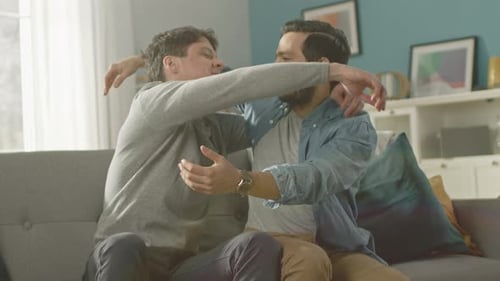 Two Men Sitting Embrace on Sofa Indoors