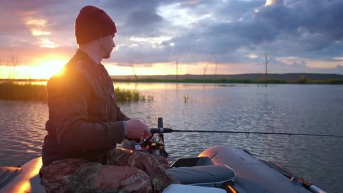 A man fishing on the lake from the boat at sunset