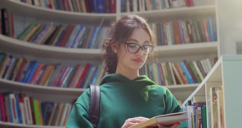 Jeune belle étudiante caucasienne portant des lunettes et un sac à dos debout dans une bibliothèque