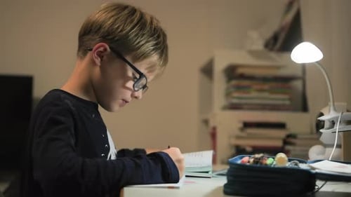 Focused Boy Completes Homework at Desk Under Lamp