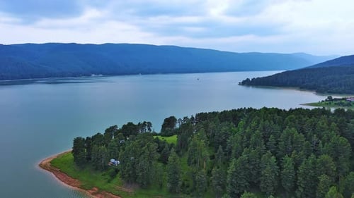 Lake with Clear Water and Stone Shore in Spruce Forest with Fir Trees Against a Daytime Sky