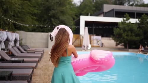 Woman Plays with Pink Flamingo Inflatable by Pool