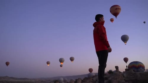 Slow motion rotating view of a man surrounded by rising hot air balloons at dawn in Cappadocia, Turk