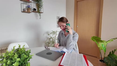 Woman Talking on Phone While Writing in Notebook