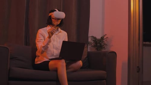 Woman Using VR Headset and Laptop on Sofa