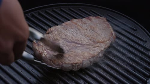 Close up of juicy beef steak flipped around with tongs on hot grill