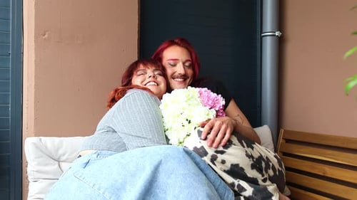 Non-binary person kissing chubby friend on a terrace