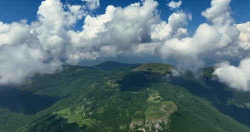 Flying trough white fluffy clouds above green mountain peaks. Beautiful summer sunny day on the high
