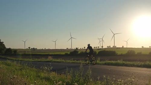 Cyclist Riding on Rural Road with Wind Turbines at Sunset