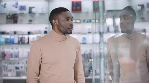 An African Man Walks Along the Glowing Windows in an Electronics Store