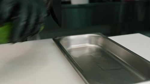 Close-up of a sushi maker in gloves cutting a cucumber with a professional kitchen knife