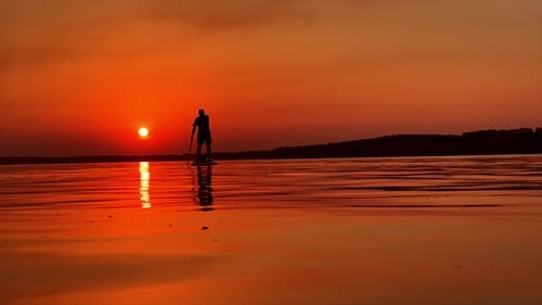 Ruhiger windstiler Abend am Fluss. Männlicher Sportler beim SUP-Boarden bei Sonnenuntergang
.