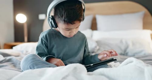 Young Boy Using Tablet in Bedroom With Headphones