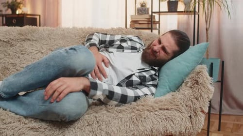 Man Lying on Couch Clutching Stomach in Discomfort