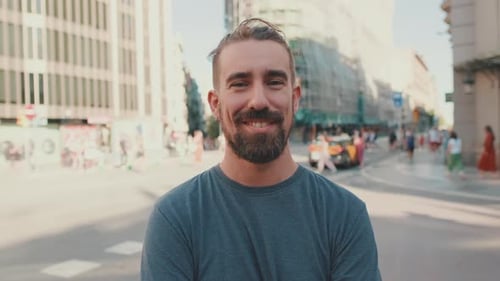 Close-up of young smiling man with beard standing in front of busy intersection