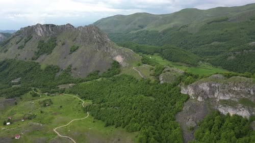 Flying over beautiful green mountains. In the background, stone cliffs with snow are visible.
