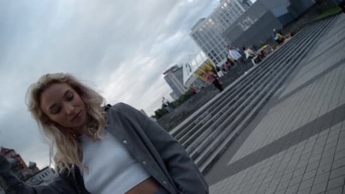 Happy Woman Posing in Big City While Touching Hair in Downtown Buildings