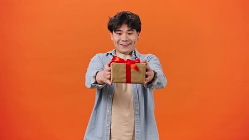 Young Adult Offering Wrapped Gift on Orange Background