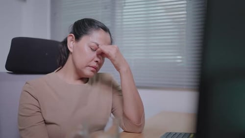 Close-up of a freelance woman at a desk using a laptop and she is stressed out taking medication t