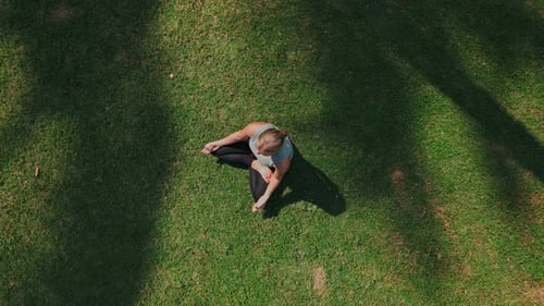 Beautiful Woman Doing Yoga Exercise and Breath Meditation Sitting on Green Grass
